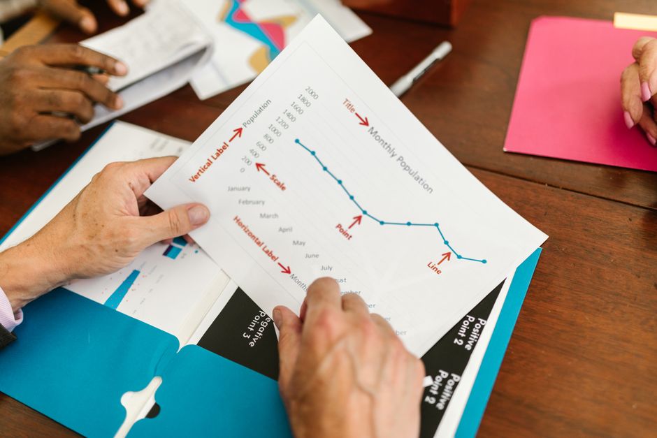 Hands examining a printed report with population and timeline chart during a business meeting.